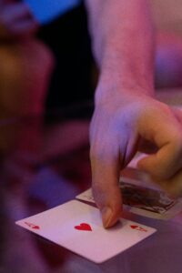 A hand holding an Ace of hearts card on a reflective table, creating a vibrant gaming atmosphere.